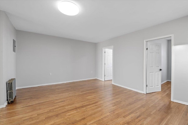 unfurnished room featuring radiator, light wood-style floors, and baseboards