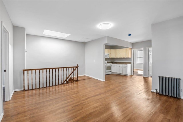 living room with baseboards, a skylight, light wood-style flooring, and radiator