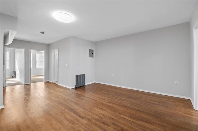 unfurnished room with baseboards, electric panel, radiator heating unit, and wood finished floors