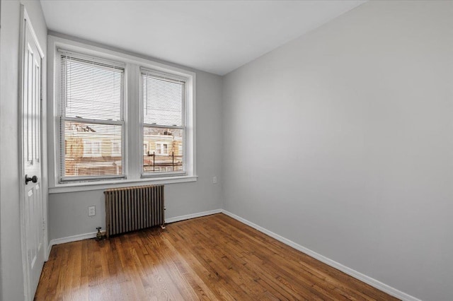 spare room featuring radiator heating unit, baseboards, and wood finished floors