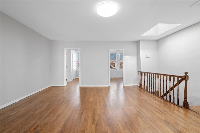 unfurnished room with a skylight, baseboards, and wood finished floors