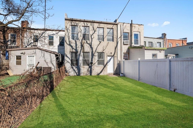 back of property with stucco siding, fence, a lawn, and an outdoor structure