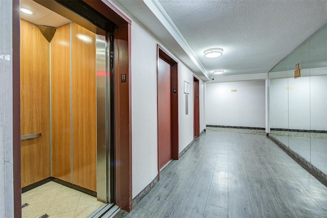 corridor with a textured ceiling, light wood finished floors, and elevator