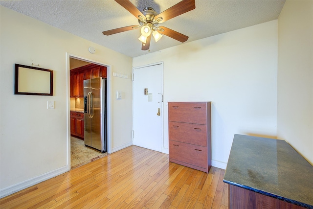 unfurnished room featuring a textured ceiling, a ceiling fan, light wood-style flooring, and baseboards