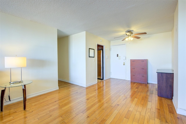 empty room with light wood-type flooring, ceiling fan, baseboards, and a textured ceiling