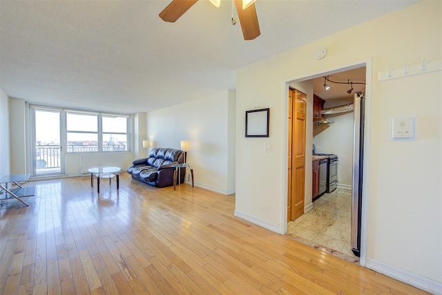 living area with a textured ceiling, a ceiling fan, light wood-style flooring, and baseboards