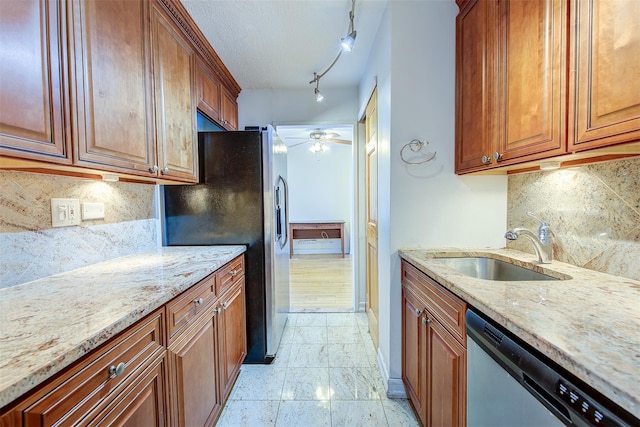 kitchen featuring ceiling fan, a sink, appliances with stainless steel finishes, light stone countertops, and brown cabinetry