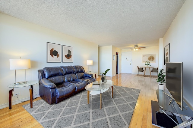 living area featuring baseboards, a textured ceiling, a ceiling fan, and wood finished floors