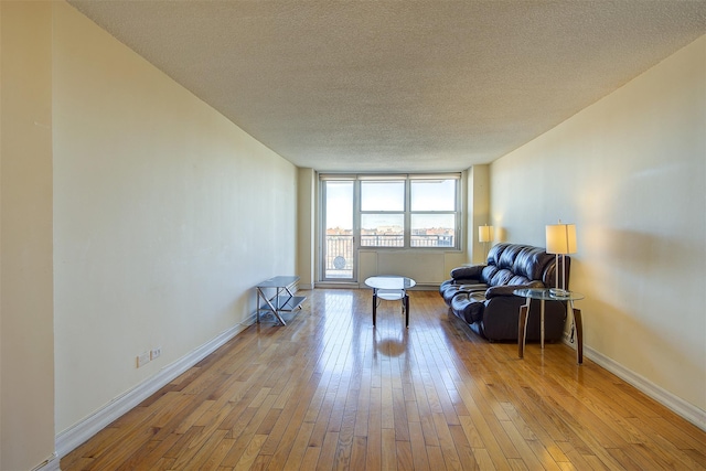 living area with baseboards, light wood-style flooring, and a textured ceiling