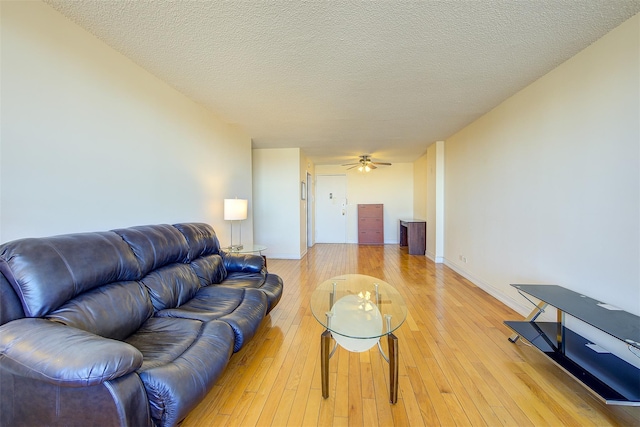 living room featuring light wood-type flooring, ceiling fan, a textured ceiling, and baseboards