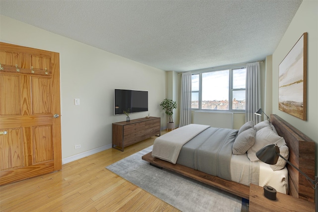 bedroom with a textured ceiling, light wood finished floors, and baseboards