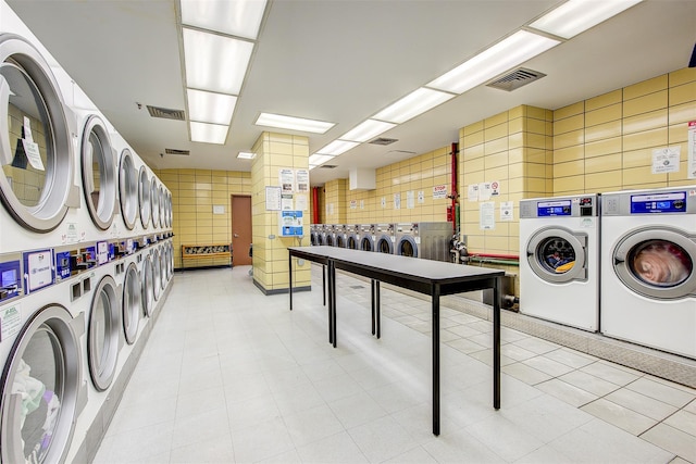 common laundry area with stacked washing maching and dryer, washing machine and dryer, visible vents, and tile walls