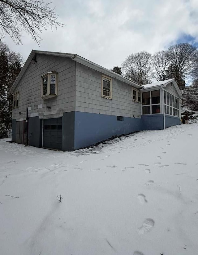 view of snowy exterior featuring a sunroom and an attached garage