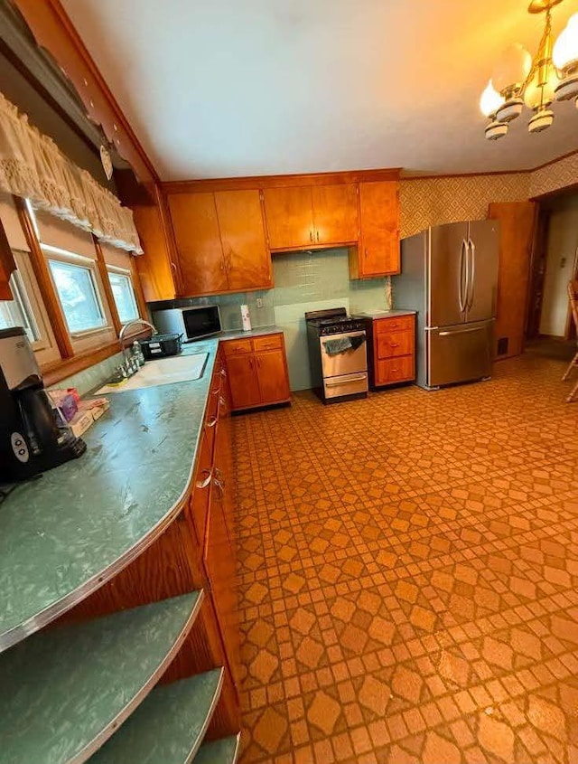 kitchen with a notable chandelier, light floors, hanging light fixtures, appliances with stainless steel finishes, and brown cabinetry