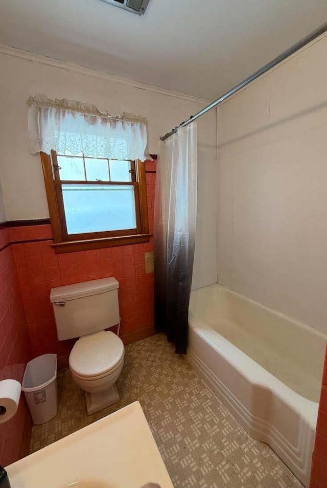 bathroom with a wainscoted wall, shower / tub combo with curtain, tile walls, toilet, and tile patterned floors