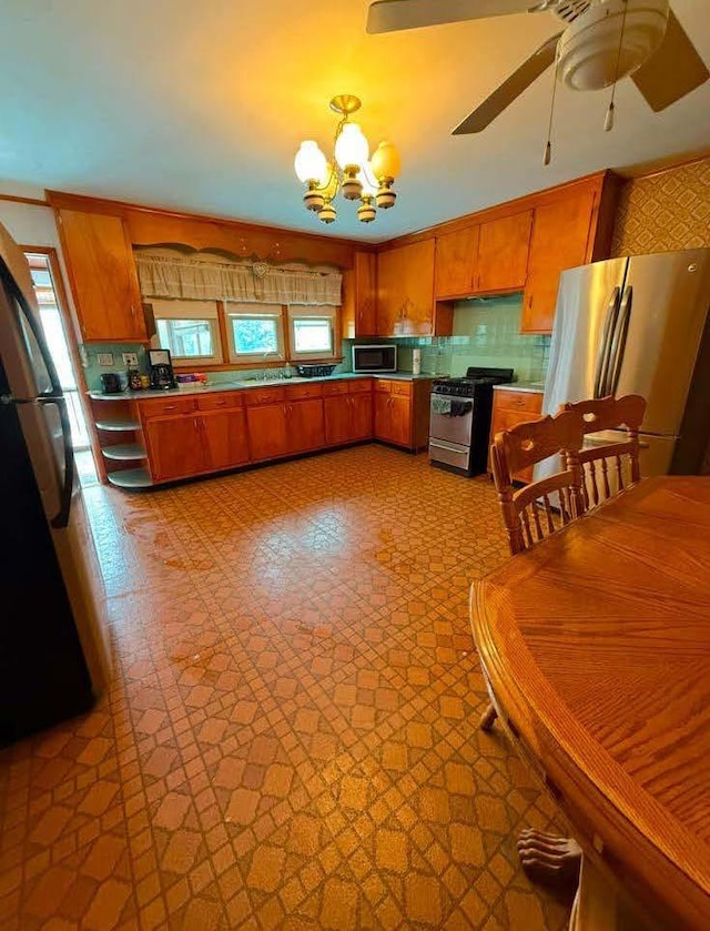 kitchen with ceiling fan with notable chandelier, appliances with stainless steel finishes, and brown cabinets