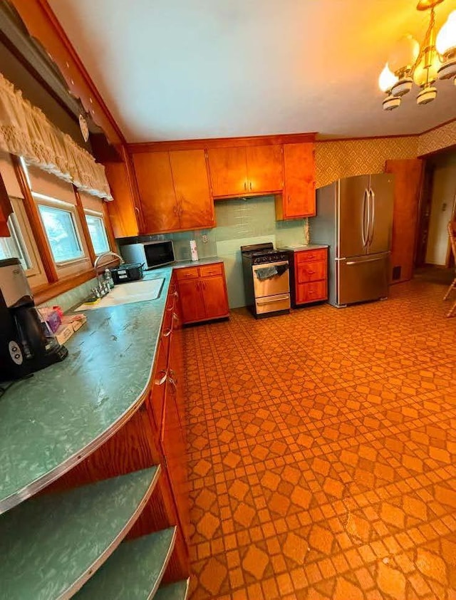 kitchen featuring a chandelier, stainless steel appliances, a sink, tile patterned floors, and brown cabinets