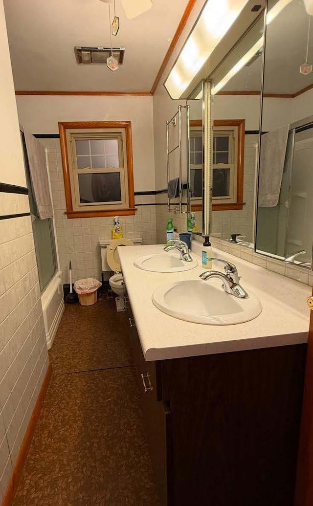 bathroom with crown molding, enclosed tub / shower combo, tile walls, and a sink