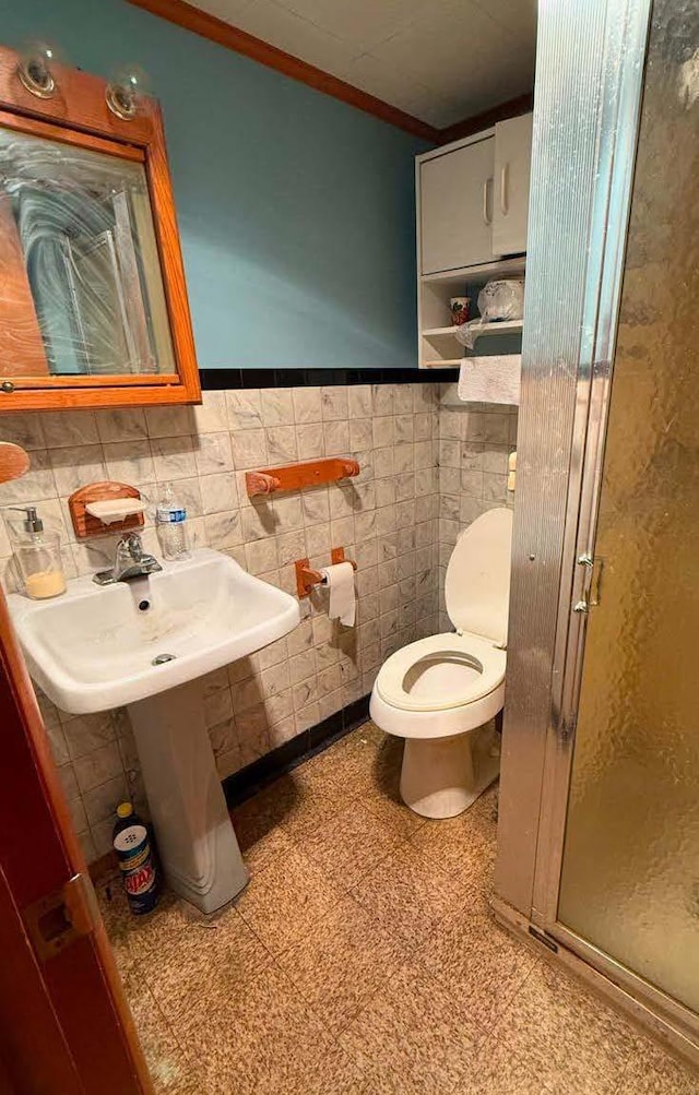 full bathroom with a stall shower, wainscoting, toilet, ornamental molding, and tile walls