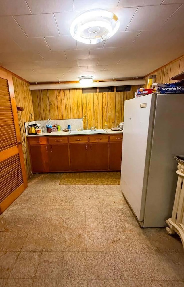 kitchen with brown cabinets, light floors, light countertops, freestanding refrigerator, and a sink