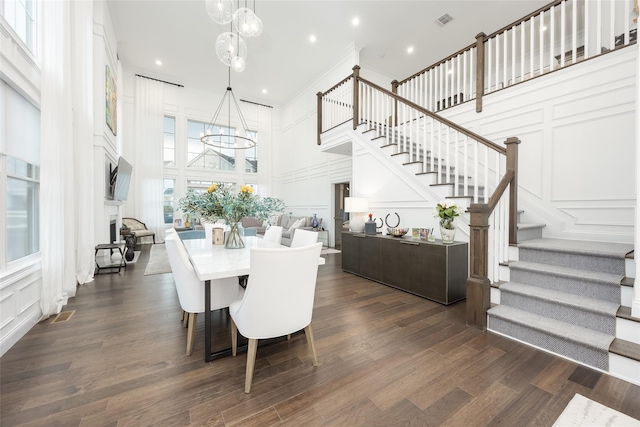 dining space featuring a notable chandelier, a decorative wall, dark wood-type flooring, visible vents, and stairs