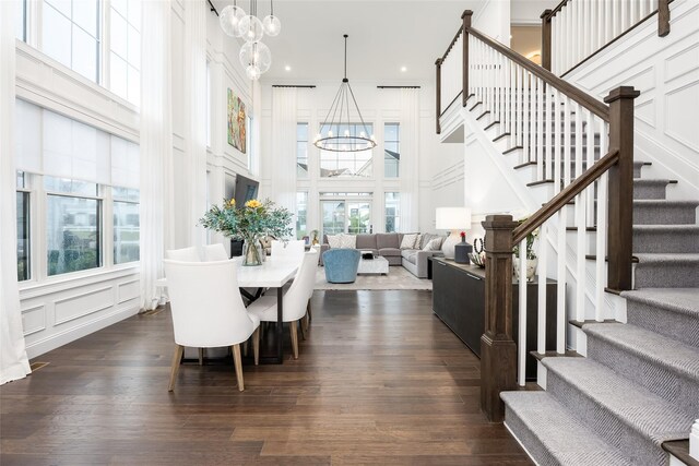 dining area featuring a chandelier, a decorative wall, a towering ceiling, stairs, and dark wood-style floors