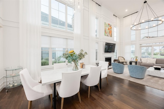 dining room featuring a towering ceiling, an inviting chandelier, a fireplace, and dark wood-type flooring