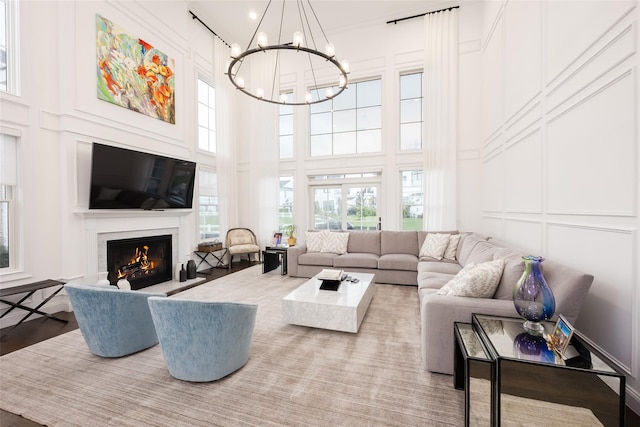 living area featuring a chandelier, a lit fireplace, a high ceiling, and a decorative wall