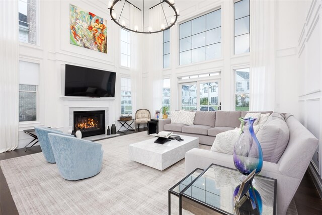 living room featuring a chandelier, a glass covered fireplace, a towering ceiling, and wood finished floors