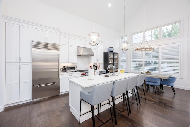 kitchen featuring built in refrigerator, under cabinet range hood, white cabinetry, and hanging light fixtures