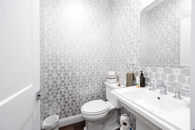 half bathroom featuring toilet, wallpapered walls, and a sink