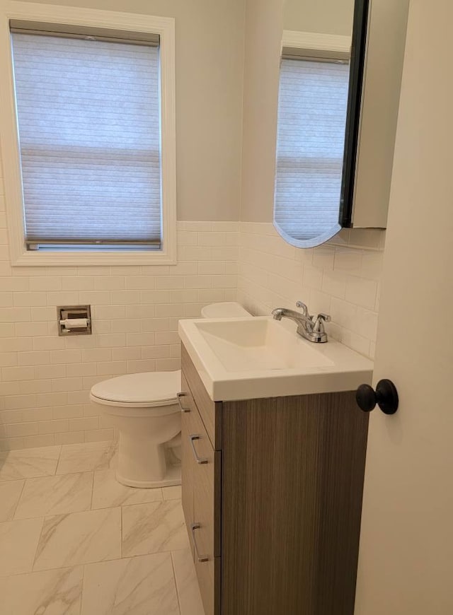 half bathroom with toilet, marble finish floor, vanity, and tile walls