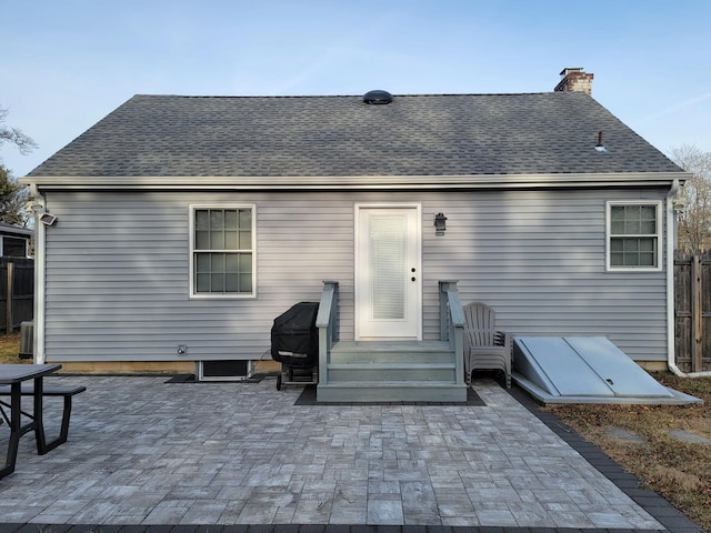 back of property with entry steps, a patio area, a chimney, and roof with shingles