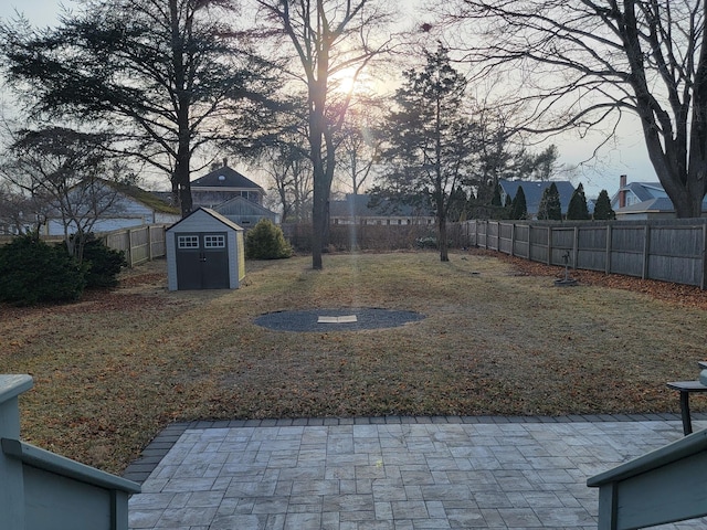 yard at dusk featuring an outbuilding, a fenced backyard, a patio, and a shed