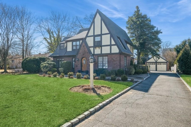 tudor home with brick siding, an outdoor structure, a detached garage, stucco siding, and a front lawn