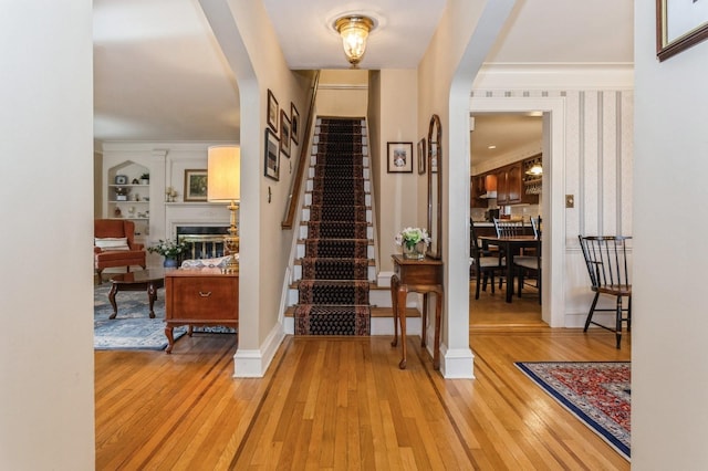 foyer entrance featuring arched walkways, baseboards, stairway, light wood finished floors, and a glass covered fireplace