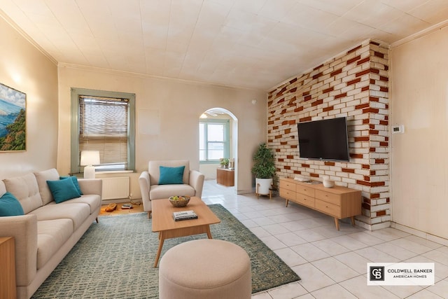 living area featuring radiator heating unit, arched walkways, crown molding, light tile patterned floors, and baseboards