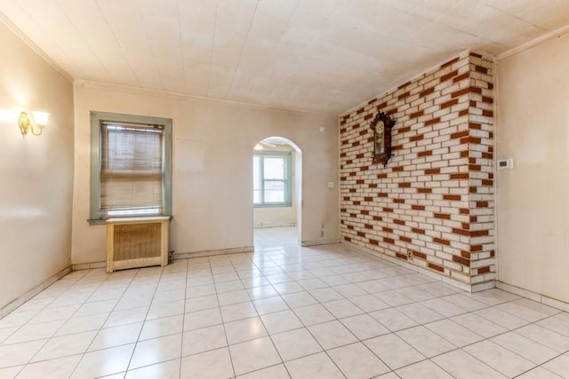 unfurnished room featuring radiator, brick wall, light tile patterned flooring, arched walkways, and crown molding