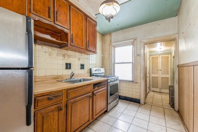 5130 47th St, Woodside, NY 11377 - kitchen with a sink, stainless steel appliances, brown cabinetry, light countertops, and light tile patterned floors