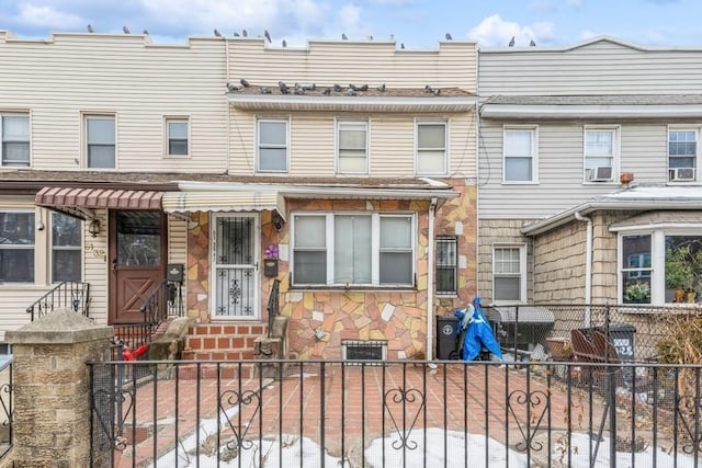 multi unit property featuring a fenced front yard, stone siding, and cooling unit