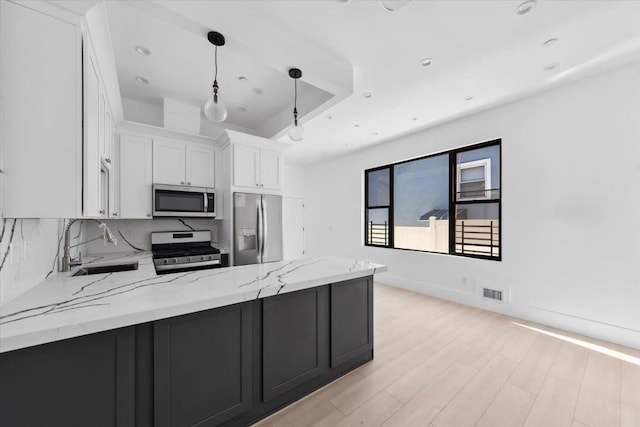 kitchen with light stone counters, a sink, white cabinetry, hanging light fixtures, and appliances with stainless steel finishes