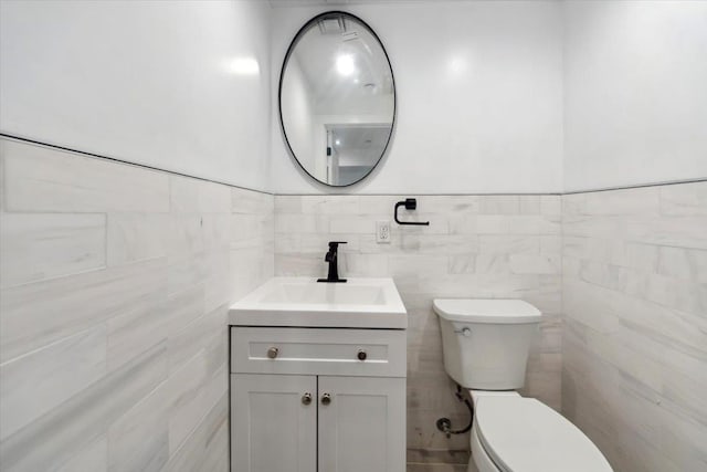 half bathroom featuring tile walls, vanity, and toilet