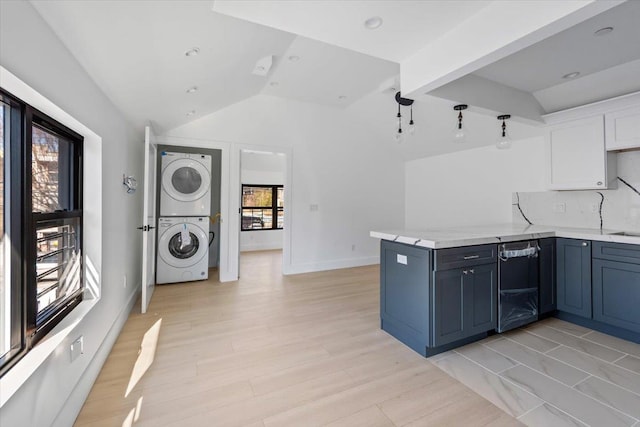 kitchen with stacked washer and clothes dryer, backsplash, white cabinets, vaulted ceiling, and a peninsula