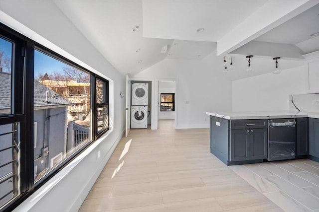 interior space with stacked washer and clothes dryer, lofted ceiling, light countertops, white cabinets, and dishwasher