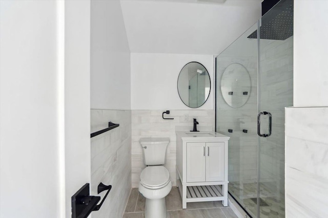 full bathroom with wainscoting, toilet, vanity, a shower stall, and tile walls