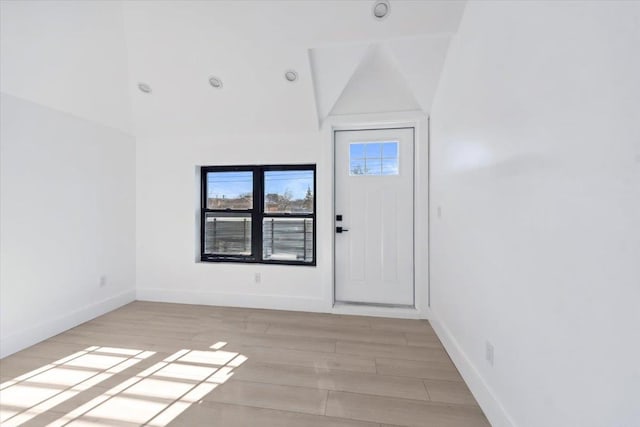 spare room with light wood-style floors, baseboards, and vaulted ceiling