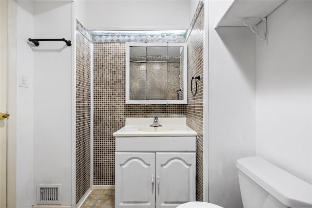 bathroom with tile walls, visible vents, vanity, and toilet