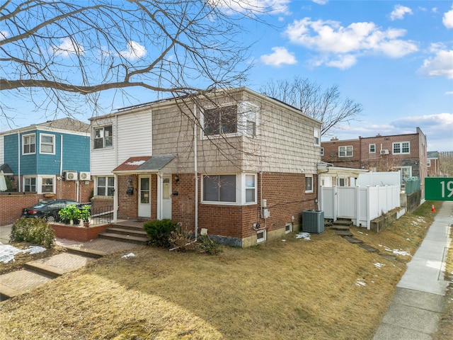 view of front of home featuring brick siding, central AC unit, fence, and a front yard