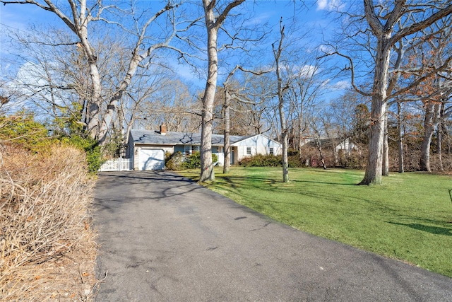 view of front facade featuring a front yard, a chimney, a garage, and aphalt driveway