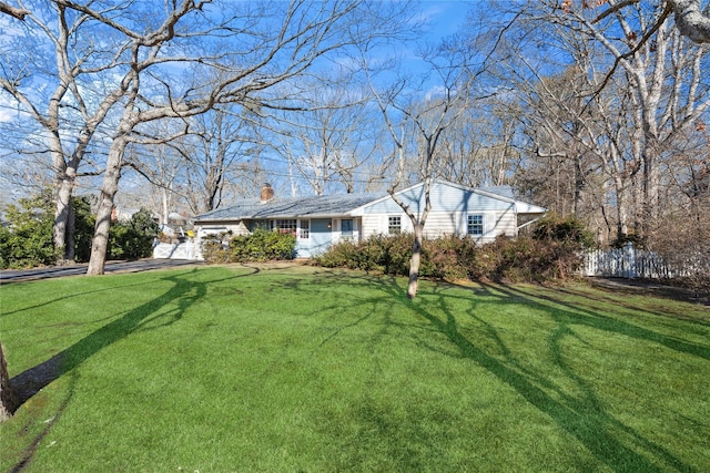 ranch-style home featuring a garage, a chimney, a front lawn, and fence